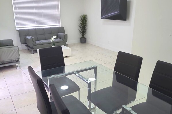 Une salle de réunion moderne avec une table en verre et des chaises noires, un canapé gris et une plante en pot.