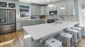 A modern kitchen with a large island, stainless steel appliances, and bar stools. - WATERSHED COTTAGE, MODERN 3BD/2BA HOME W/POOL & FIRE PIT! PET FRIENDLY! (Mexico Beach)