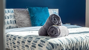 Un lit bien fait, avec une literie à motifs, un coussin turquoise et des serviettes enroulées.