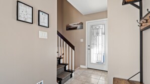 Un couloir avec un escalier, une porte dotée d’un panneau en verre et une étagère fixée au mur, sur laquelle se trouve un panier.