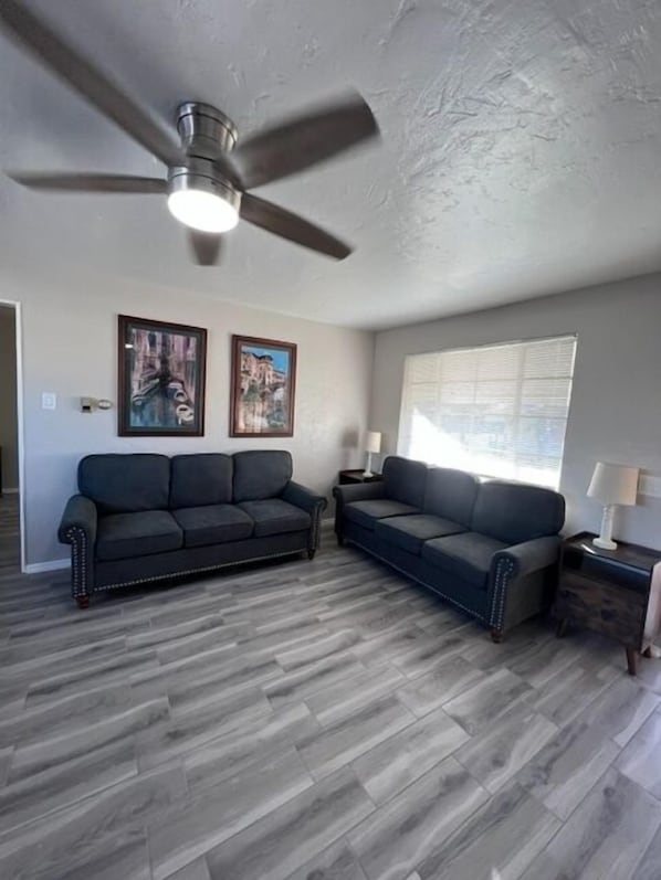 A living room with two dark sofas, a ceiling fan, and a window with blinds. - Tucson Rincon Heights 1BR with Parking (Tucson)