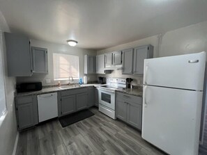 A compact kitchen with grey cabinets, a white refrigerator, a stove, and a microwave. - Tucson Rincon Heights 1BR with Parking (Tucson)