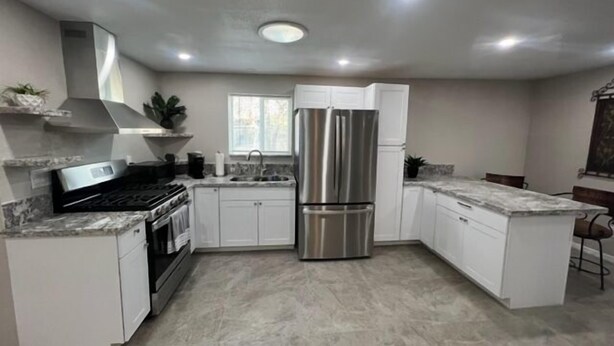 A modern kitchen with white cabinets, a stainless steel refrigerator, a built-in oven, and a granite countertop.