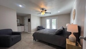A bedroom with a bed, a chair, a ceiling fan, and a nightstand with a lamp.
