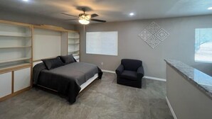 Ein Schlafzimmer mit Bett, Stuhl, Deckenventilator und eingebauten Regalen.