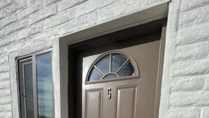 Eine beigefarbene Haustür mit der Zahl 5 darüber, einem kleinen Fenster links und einer Fußmatte am Eingang.