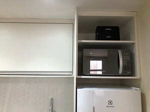 A kitchen with a white refrigerator, a black microwave, and a white cabinet.