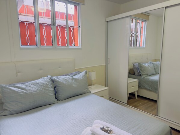 A bedroom with a bed, bedside table, nightstand, and a wardrobe.