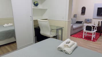 Quarto de hotel com cama, escrivaninha e cadeira, sofá, mesinha e outra cadeira, e um tapete vermelho.