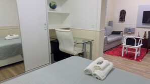 Een hotelkamer met een bed, een bureau met stoel, een bank, een klein tafeltje met stoel, en een rood vloerkleed.