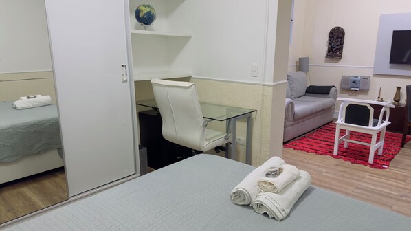 A hotel room with a bed, a desk with a chair, a sofa, a small table with a chair, and a red rug.