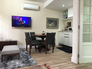 A dining area with a TV, chairs, a table, and a kitchen in the background.