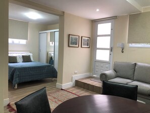 A bedroom with a bed, a sofa, a dining table, and a door with a window.