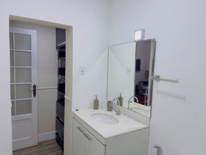 Een badkamer met een wit wastafel, een spiegel en een deur naar een inloopkast.
