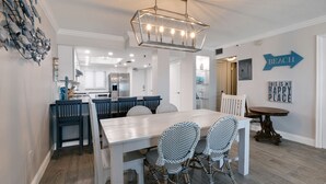 A modern kitchen with white cabinets, a central island, and a dining area with a white table and wicker chairs.