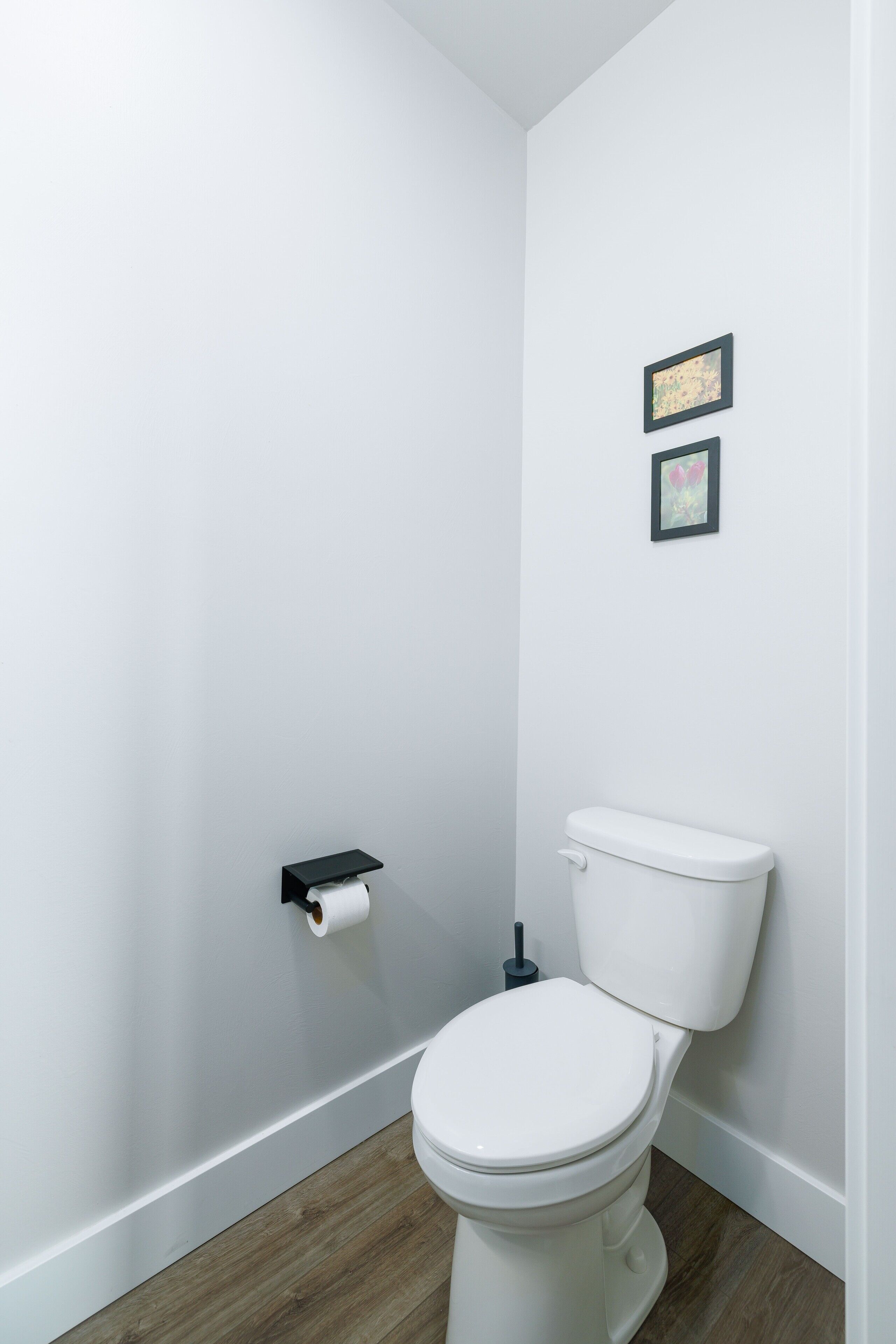 A small, modern bathroom with a white toilet, a wooden floor, and two framed pictures on the wall.