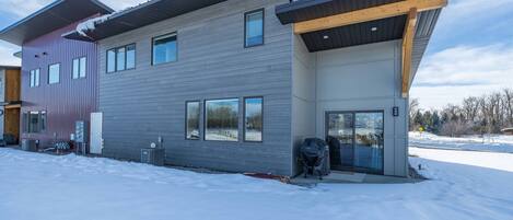 A modern two-story house with a grey exterior, a wooden deck, and a garage.