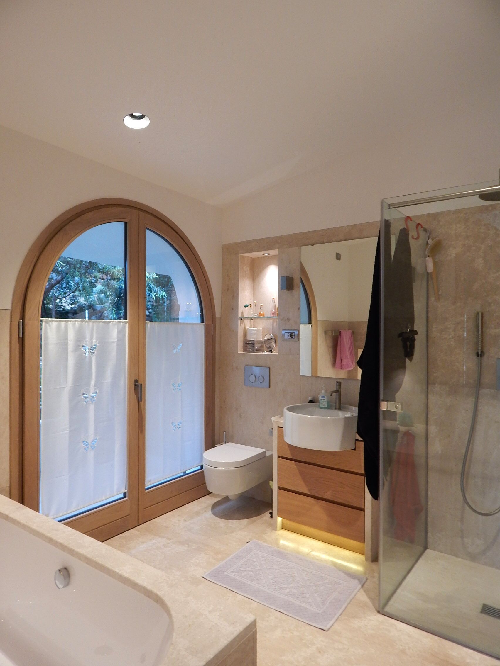 Une salle de bain moderne dotée d’une grande fenêtre, d’une douche, de toilettes et d’un lavabo.
