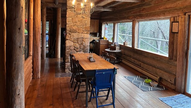 L’intérieur d’un chalet rustique, avec une cheminée en pierre, une table à manger en bois et de grandes fenêtres.