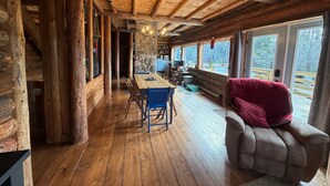 L'intérieur d'une cabane en rondins, avec une table à manger en bois, des chaises bleues, un canapé rouge, des murs en pierre et de grandes fenêtres.