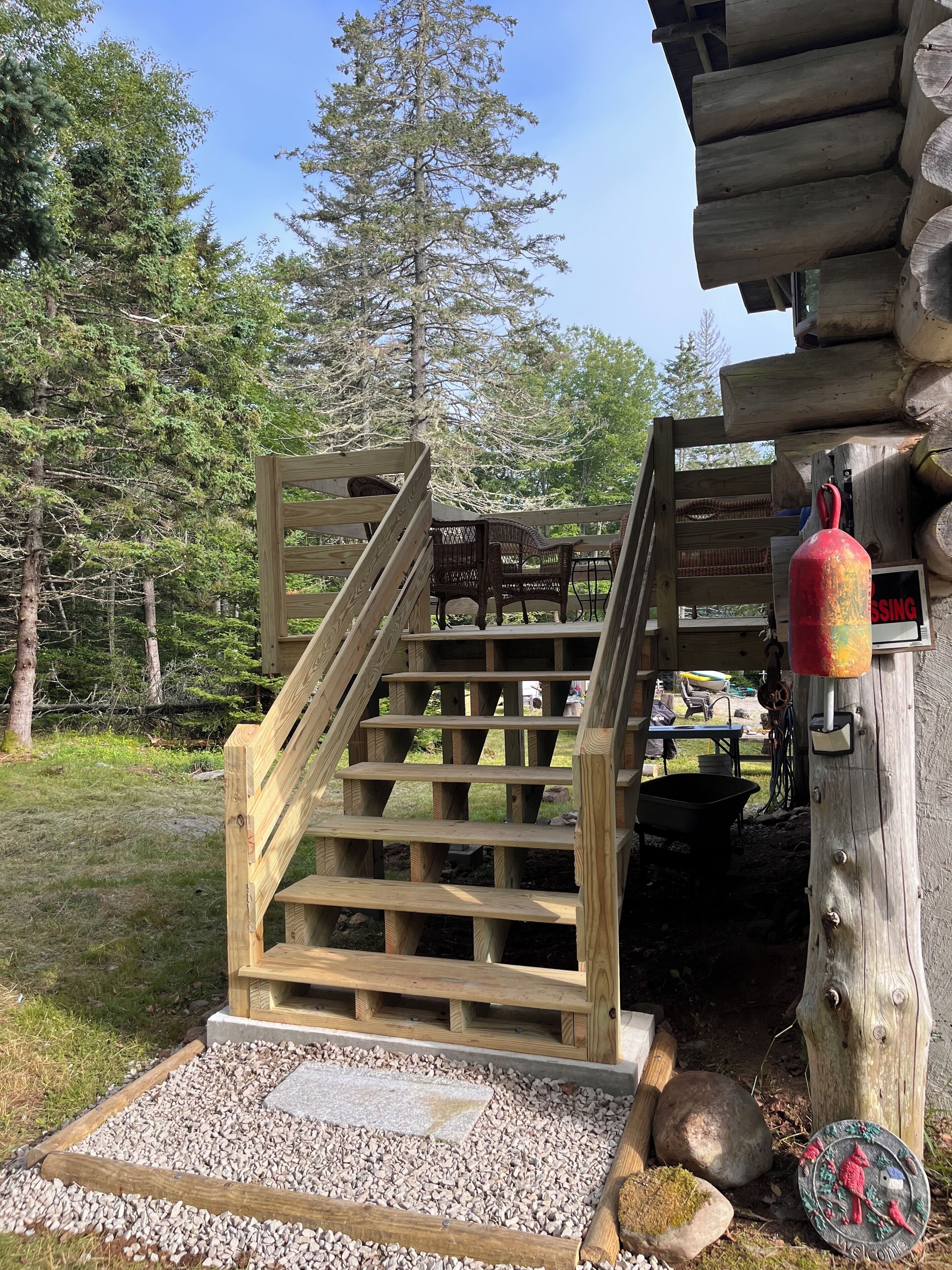 A wooden staircase leading to a cabin entrance, surrounded by a gravel path and a wooden deck.