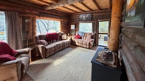 L’intérieur d’une cabane en rondins, avec un ensemble de canapés, une cheminée et un téléviseur fixé au mur.