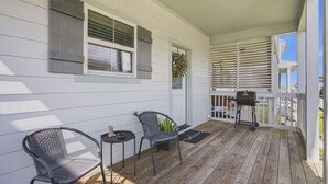 A covered porch with two chairs, a small table, a grill, and a potted plant.