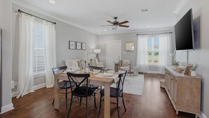 A dining area with a wooden table and chairs, a ceiling fan, and a TV mounted on the wall.