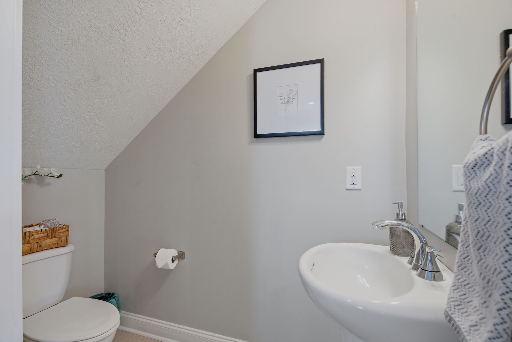 A bathroom with a white toilet, a sink with a mirror, and a framed picture on the wall.