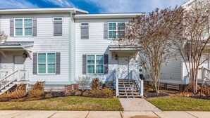 A two-story residential building with a front porch, a small staircase, and a well-maintained lawn.
