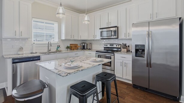 A modern kitchen with white cabinets, stainless steel appliances, a granite countertop, and pendant lighting.