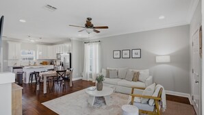 A modern living room with a white sofa, a coffee table, and a dining area with chairs and a table.