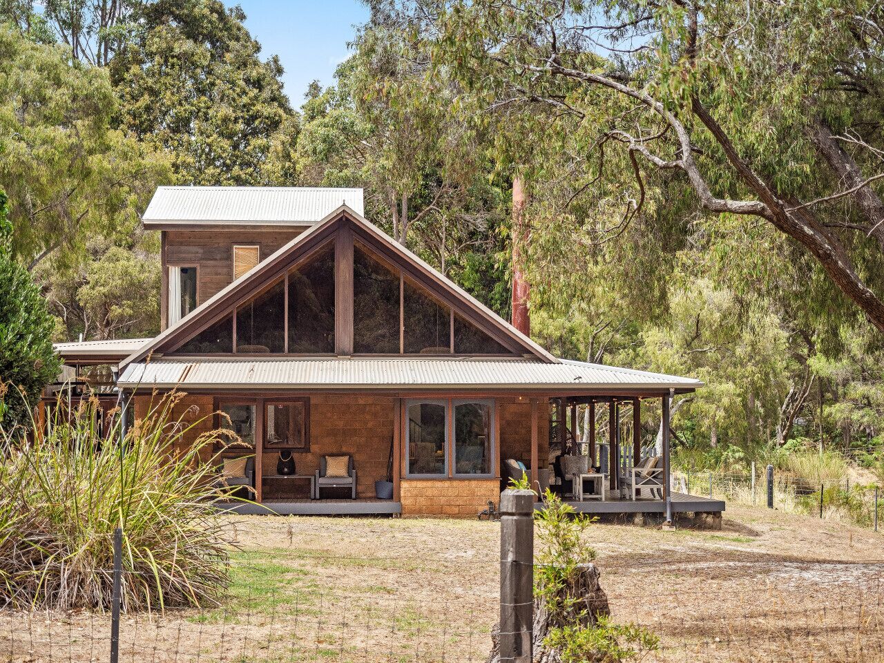 A two-story house with a large porch, surrounded by trees and a fenced yard.