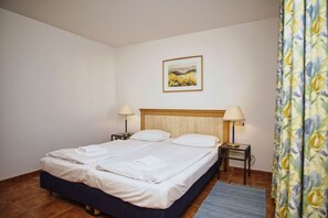A hotel room with a bed, two bedside tables, a lamp on each table, a painting on the wall, and a floral curtain.
