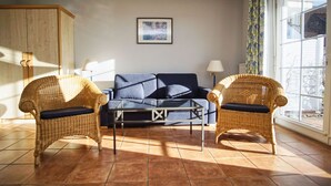 Ein Wohnzimmer mit einer Couch, zwei Korbstühlen, einem Couchtisch und einem Fenster mit Vorhängen.