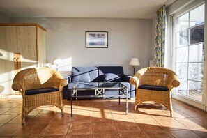 Ein Wohnzimmer mit einer Couch, zwei Korbstühlen, einem Couchtisch und einem Fenster mit Vorhängen.