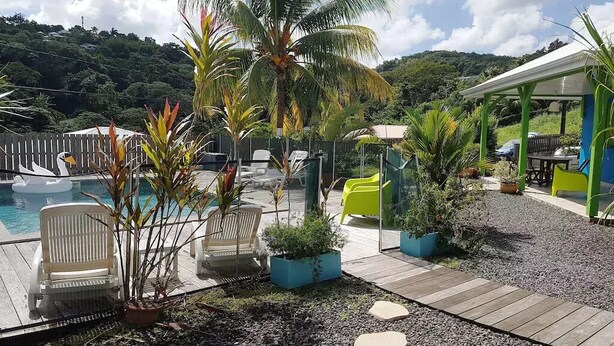 Un área de piscina con sillas de descanso, plantas en macetas y una zona de estar cubierta.