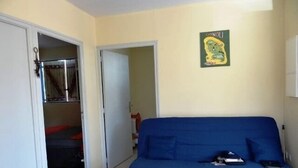 Una habitación con un sofá azul, una puerta que da a otra estancia, y una pared con un póster de un personaje de dibujos animados.