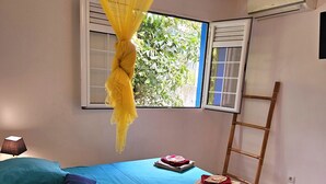 Un dormitorio con cama, una mesita de noche con lámpara, un control remoto y una escalera apoyada en la pared.