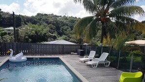 Una piscina con un flotador con forma de cisne, rodeada por una terraza de madera y sillas de descanso blancas.