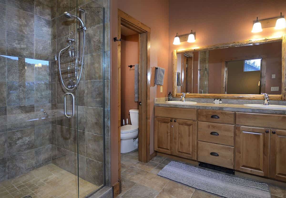 Une salle de bain avec une douche à parois de verre, un meuble-lavabo en bois doté d’un grand miroir et des toilettes.