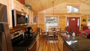 Ein Holzhütten-Interieur mit einer Küche, die Edelstahlgeräte, einen Essbereich mit Holzmöbeln und eine rote Tür zeigt.