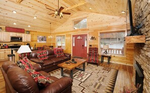 A cozy log cabin interior with a leather sofa, wooden coffee table, and a fireplace. - Livin' Good - Hot Tub, Resort Pool & Single-Level Mountain Cabin (Gatlinburg)