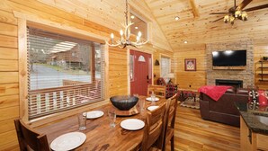 Ein Holzblockhaus-Interieur mit Essbereich, Wohnzimmer mit Kamin und Fernseher an einer Ziegelwand.
