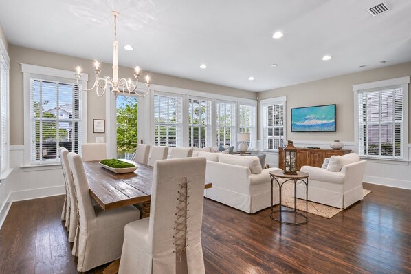 A spacious living area with a dining table, sofas, and a chandelier.