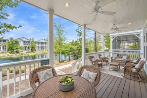 A covered outdoor area with a dining table, wicker furniture, and a view of a lake and buildings.