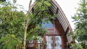 A wooden house with a curved roof, surrounded by lush greenery and a staircase leading to a deck. - Miracle Signature Hills (Ciater)