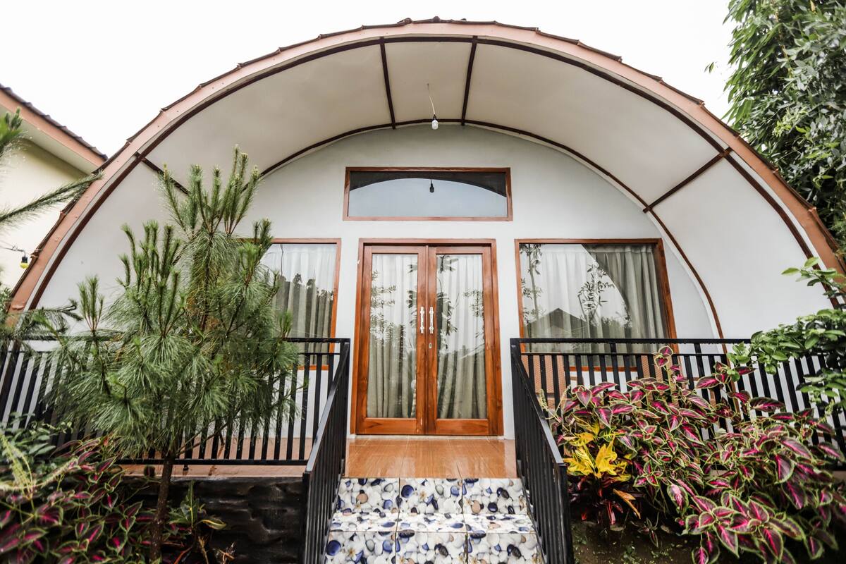 A two-story house with a curved roof, a wooden front door, and a small porch with steps.