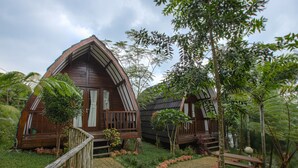 Two wooden cabins with pitched roofs surrounded by lush greenery and a wooden pathway. - Miracle Signature Hills (Ciater)