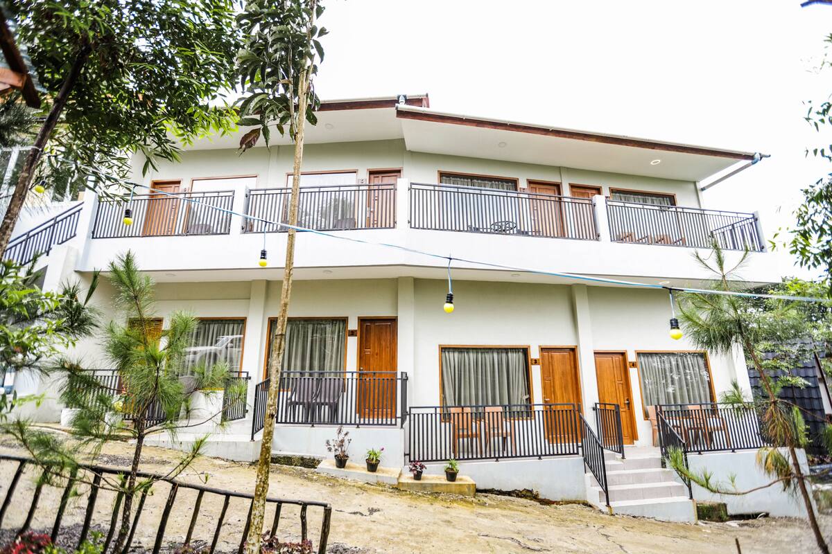 A two-story building with balconies, potted plants, and a staircase leading to the entrance.
